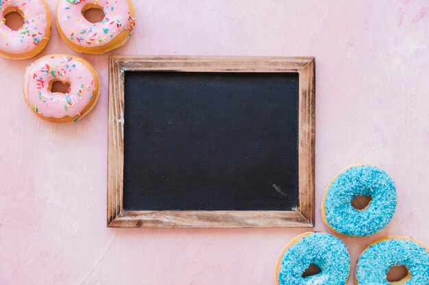 High angle view of fresh donuts with blank black slate on pink backdrop