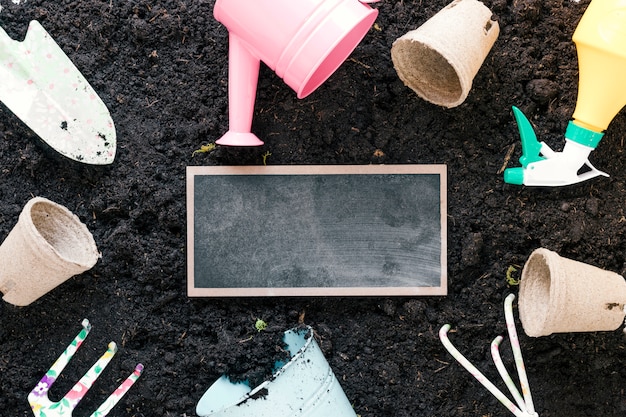 High angle view of gardening tools and blank slate arranging over black dirt