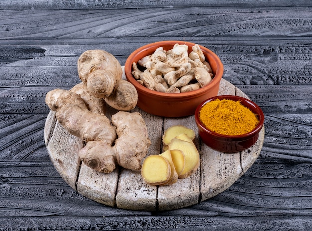 High angle view ginger in bowls with ginger slices and powder on wood and dark wooden background.