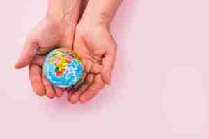 Free photo high angle view of a globe on hands against pink surface