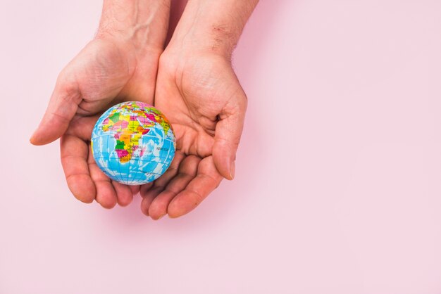 High angle view of a globe on hands against pink surface
