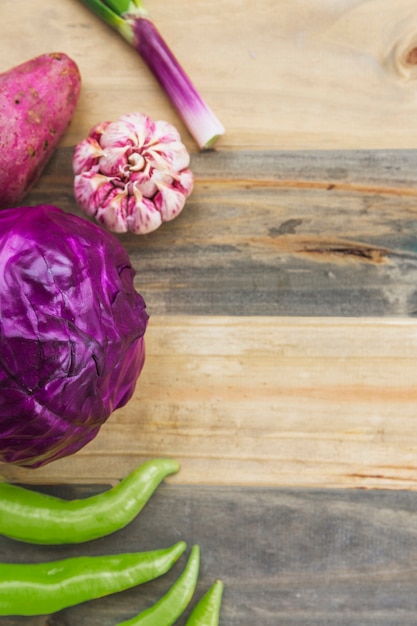 Free photo high angle view of green chili pepper; purple cabbage; garlic and sweet potato on wooden plank