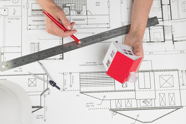 High angle view of hand holding small house model and pencil over blueprint