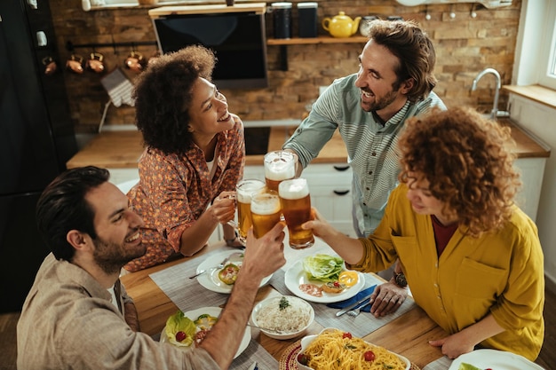 一緒に昼食をとり、ダイニングテーブルでビールと乾杯している幸せな友人の高角度のビュー。