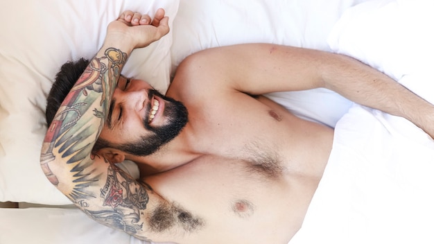 Punto di vista dell'angolo alto di un uomo senza camicia felice che dorme sul letto