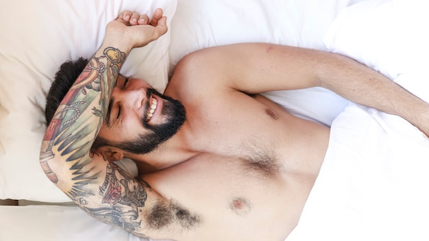 High angle view of a happy shirtless man sleeping on bed