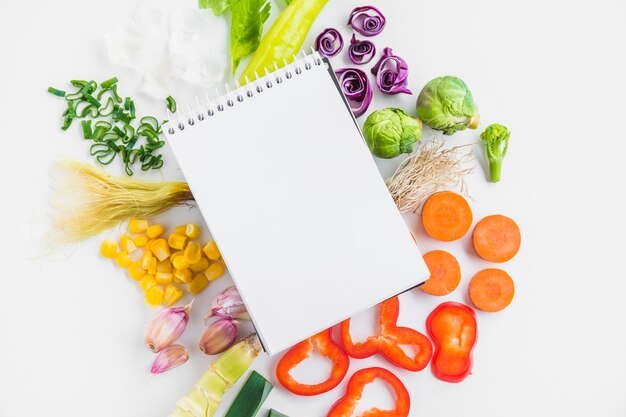 High angle view of healthy raw vegetables and spiral notepad