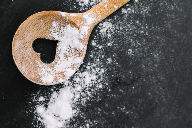 High angle view of heart shape spoon and flour on black background