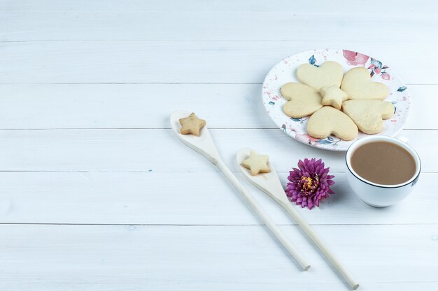 ハイアングルビューハート型クッキー、花とコーヒーのカップ、白い木の板の背景に木のスプーンで星のクッキー。水平