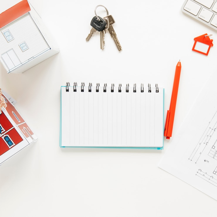 Free Photo high angle view of house model near spiral notepad with keys and pen over white background