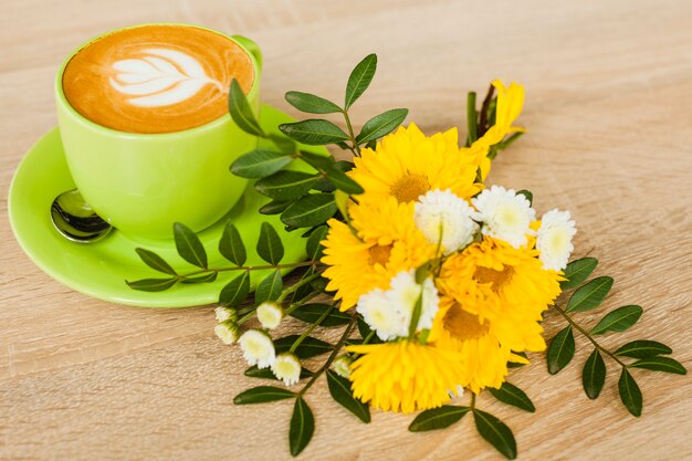 나무 질감 배경 위에 신선한 꽃과 라떼 아트 커피 컵의 높은 각도보기