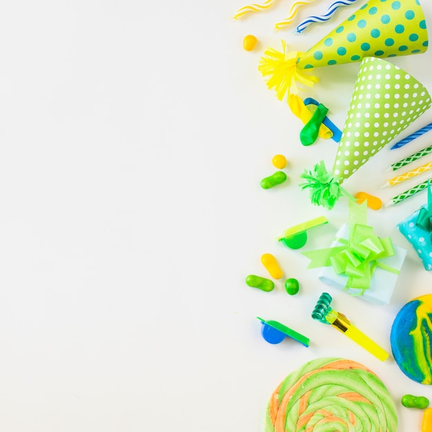 High angle view of lollipops; candies; candles; party horn blower; whistle and hat on white backdrop