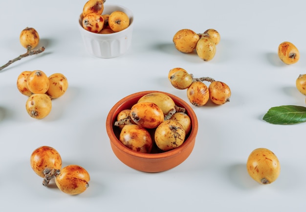 Foto gratuita loquat di vista dell'angolo alto in ciotole e su fondo bianco. orizzontale