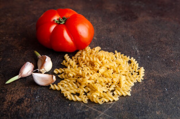 High angle view macaroni with tomato and garlic on dark textured background. horizontal