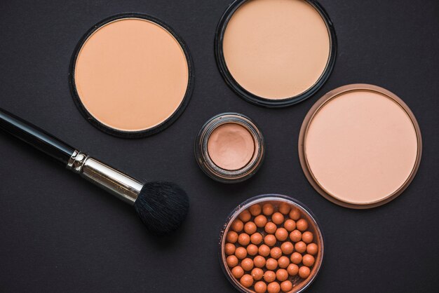High angle view of make up products with brush on black backdrop