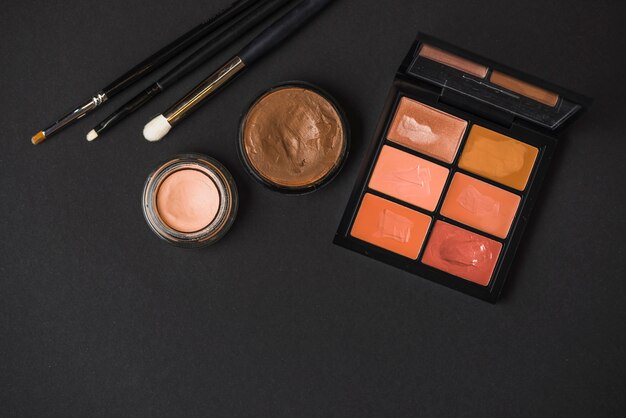 High angle view of makeup products with brushes on black backdrop