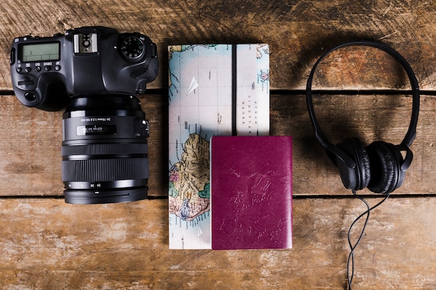 木製の背景に地図、パスポート、ヘッドホン、DSLRカメラの高い角度のビュー