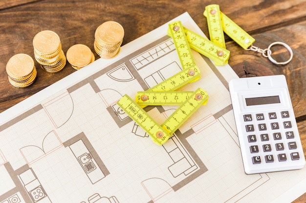 High angle view of measure tape, calculator, stacked coins and blueprint