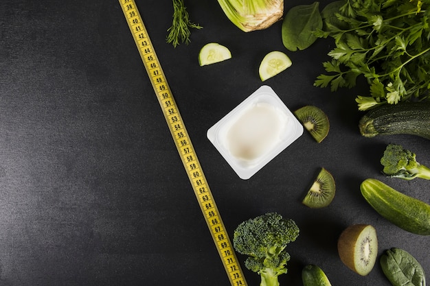 High angle view of measuring tape and vegetables on black backdrop