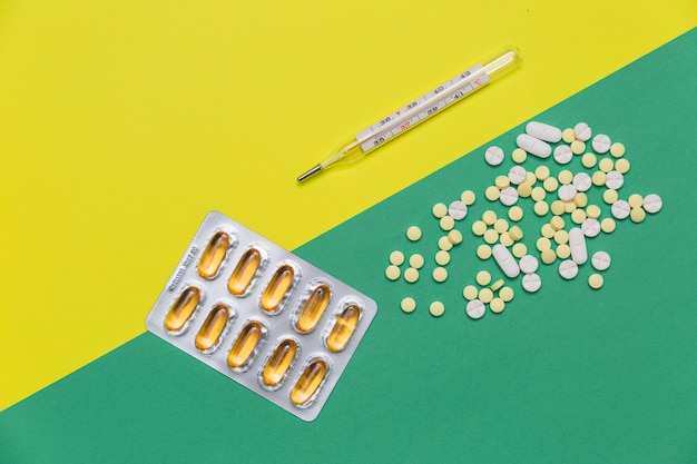 High angle view of medicines and thermometer on dual colored background