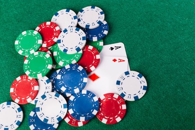 High angle view of multi colored poker chips and two aces playing cards on green surface