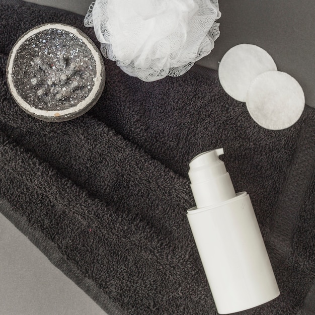 High angle view of body scrub; sponge; loofah; cosmetic bottle and towel