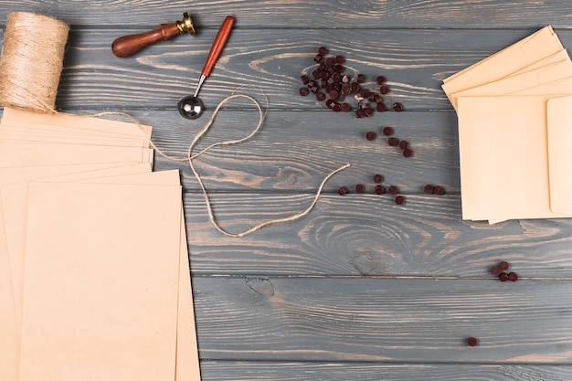 Бесплатное фото Высокий угол обзора коричневого воска; шпуля для струн; печать печатью; пустой конверт на деревянный стол