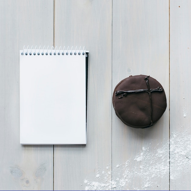 Бесплатное фото Высокий угол зрения шоколадного макароны и пустой блокнот на деревянной доске