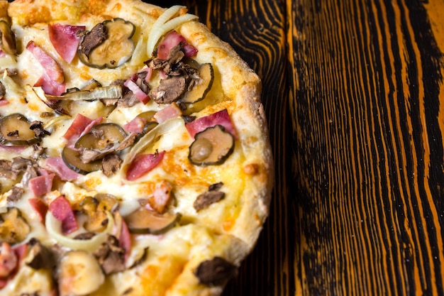 나무 테이블에 햄, 버섯, 양파, 피클을 넣은 맛있는 피자 절반의 높은 각도 보기