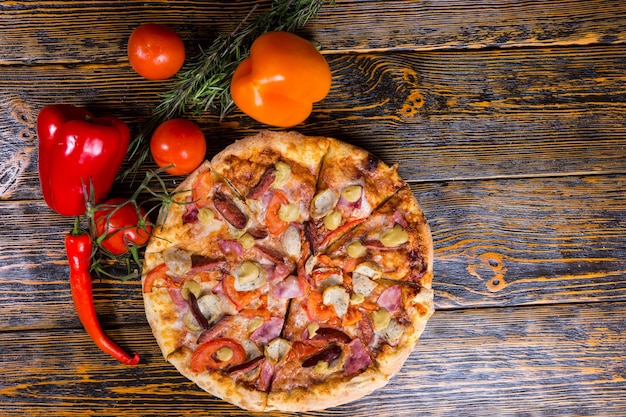 近くにソーセージがあるピザの高角度のビューは、木製のテーブルにピーマン、トマト、ローズマリーの小枝です Premium写真