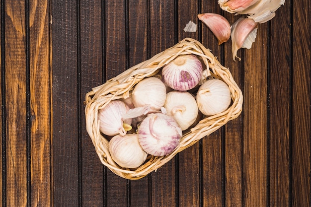 Free photo high angle view of onions in basket near garlic cloves on wooden background