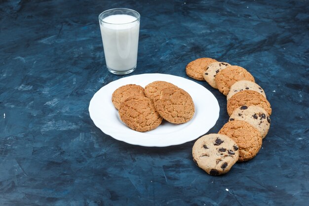 High angle view peanut butter cookies in white plate with milk, different types of cookies on dark blue background. horizontal