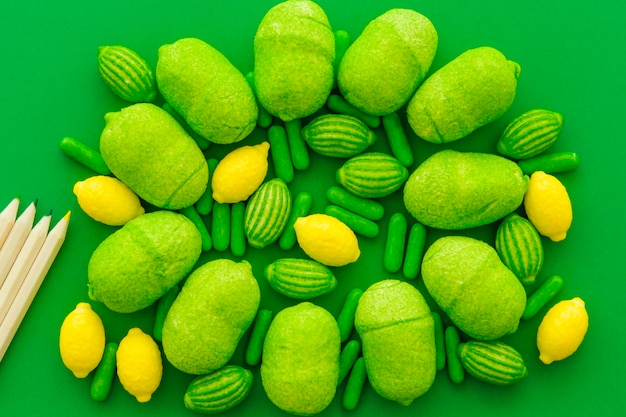 High angle view of pencils and various sweet candies on green backdrop