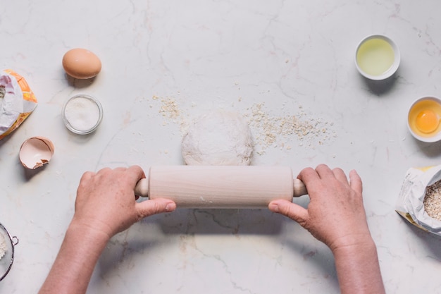 High angle view of a person's hand flattening dough with rolling pin
