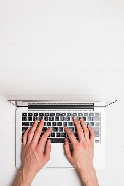 High angle view of a person's hand working on laptop over wooden desk