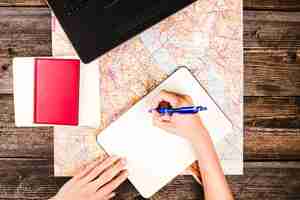 Free photo high angle view of a person's hand writing on notepad with map on table