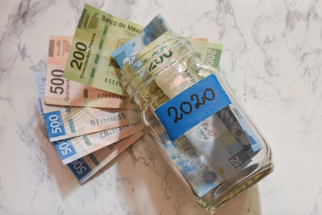 High angle view of pesos in a jar with a blue [2020] label on it on the table under the lights