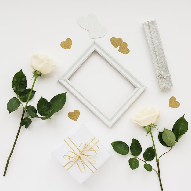 High angle view of picture frame; roses; gift and heart shape stickers on white surface