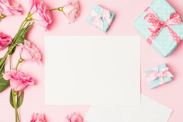 High angle view of pink flower; white blank paper and decorative gift box