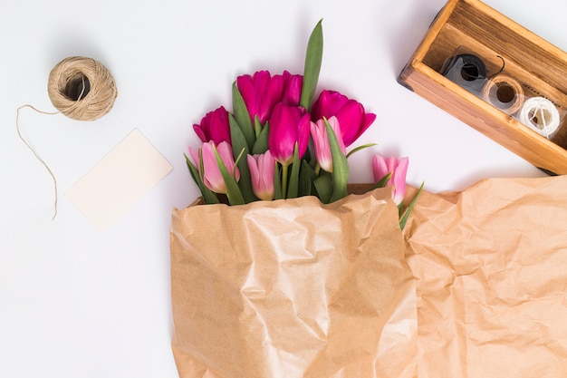 Free photo high angle view of pink tulip flowers in brown paper; with variety of strings against white background