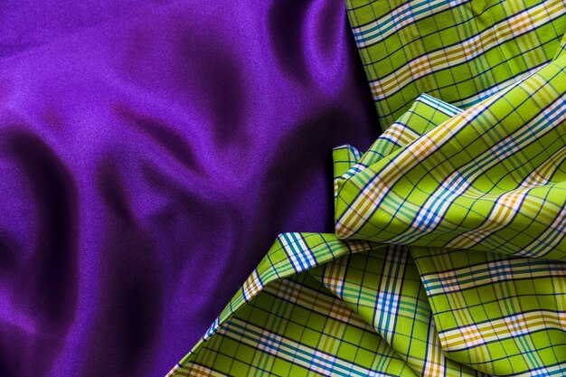 High angle view of plaid cotton cloth on plain purple textile