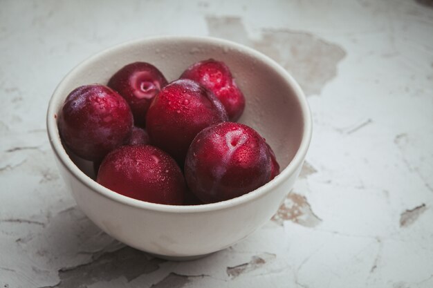 High angle view plums in bowl on white textured.