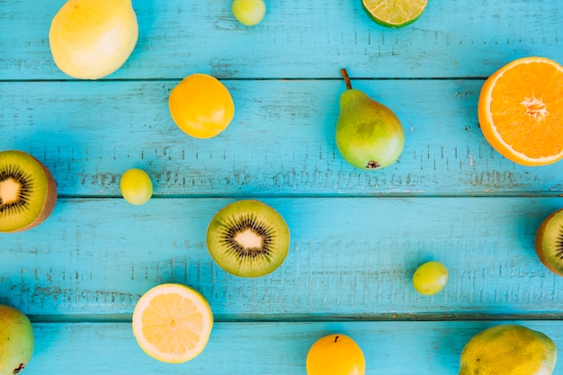 High angle view of plums; pear; grape; kiwis and citrus fruits on blue wooden plank