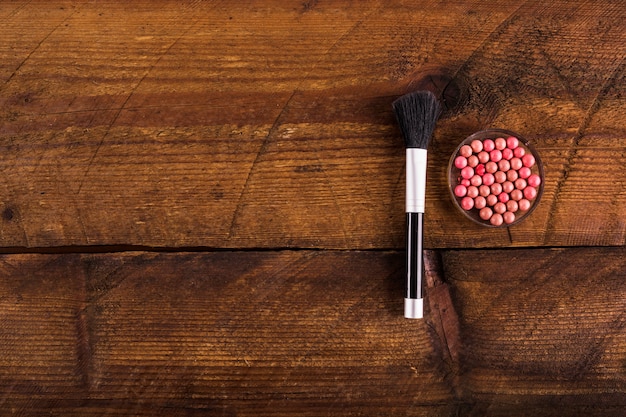 High angle view of powder balls and makeup brush on wooden backdrop