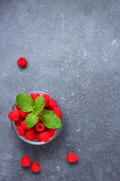 High angle view raspberries in saucer with mint leaves on gray textured table