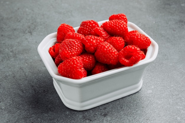 High angle view raspberries in square bowl on gray textured background. horizontal