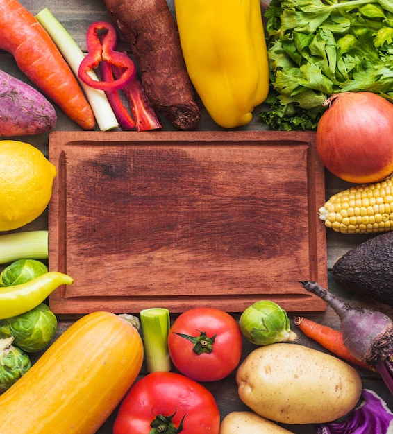 High angle view of raw vegetables surrounding wooden chopping board