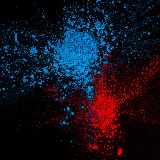 High angle view of red and blue splatted holi powder above black background