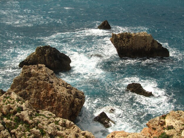 High angle view of rocks surrounded by the wavy sea under the sunlight at daytime in Malta