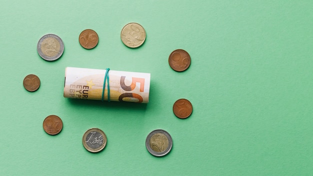 High angle view of rolled up euro bank note with coins on green background